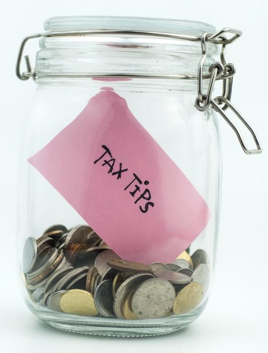 Jar filled with coins and a pink note in it with the word "Tax Tip" written on the note.