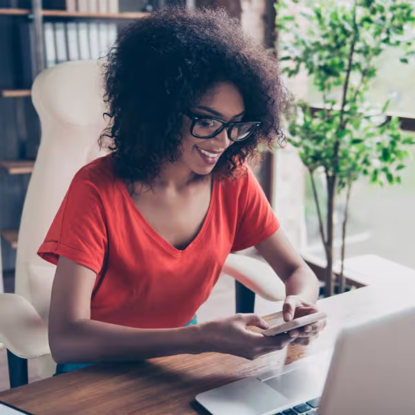 Woman checking her phone while working on a computer in an office