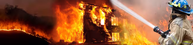 Fire fighter spraying water with hose on burning building wildfire.