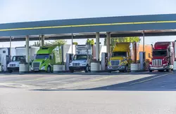 Five semi trucks lined up filling up with gasoline at fuel pumps